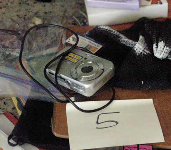 Zoom — Sony Cybershot placed on cluttered countertop with a cord draped over it